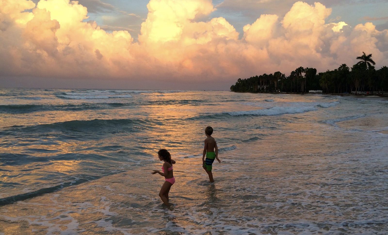 Two children playing in the ocean at sunset.